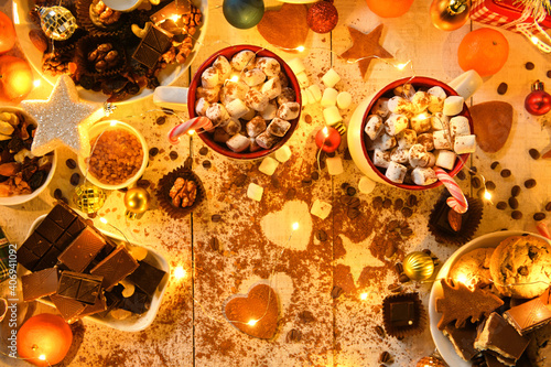 sweet food top view background for merry christmas or new year holiday decoration with night illumination - chocolate candies, tangerines, cookies, marshmallow and cocoa latte on white wood © soleg