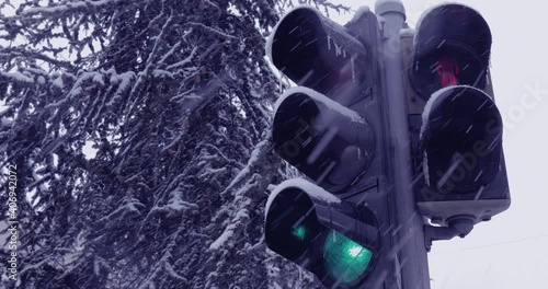 Snow falling over the frozen traffic light. Icy danger.