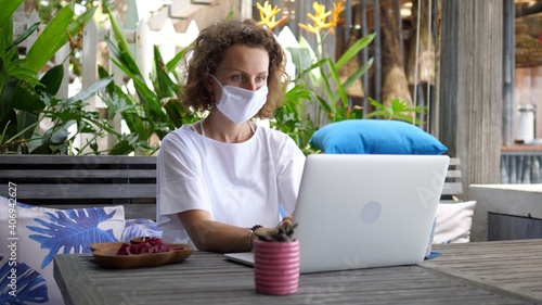 Working from anywhere concept. Young remote female worker with a laptop in tropical redtaurant photo