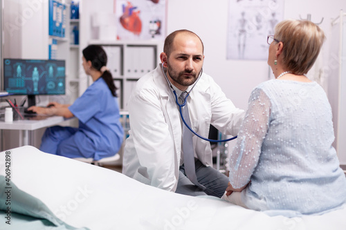 Doctor checking breathing problem of sick senior woman in hospital. Medical practitioner examining lungs of caucasian in modern clinic dressed in white coat.
