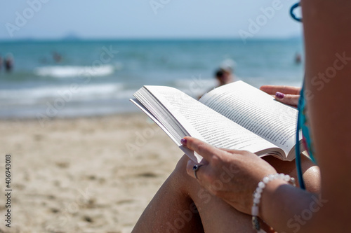 Woman reading a book on the beach, blurred background. Summer leisure on the beach