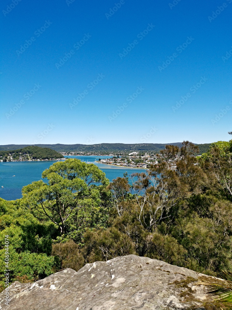 Beautiful view of a bay full of boats with tall tree in the foreground and mountains, trees and deep blue sky in the background, Allen Strom Lookout, Brisbane Water, Rocky Point Trail, New South Wales