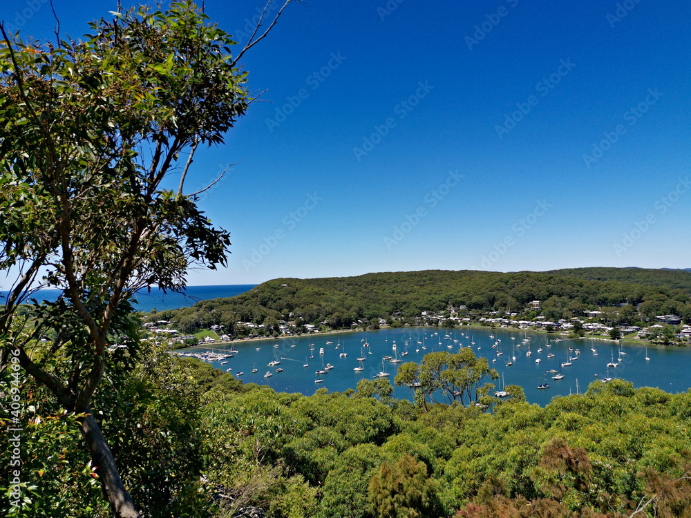 Beautiful view of a bay full of boats with tall tree in the foreground and mountains, trees and deep blue sky in the background, Allen Strom Lookout, Brisbane Water, Rocky Point Trail, New South Wales