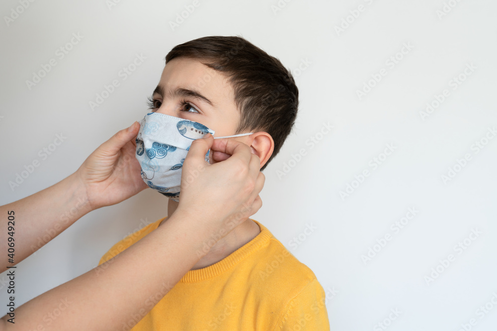 mother wears a mask on her son. woman helps to child. boy wears colorful protective medical face mask isolated white background portrait photo. during coronavirus outbreak. 2021 pandemic lockdown. mother wears a mask on her son. woman helps to child. boy wears colorful protective medical face mask isolated white background portrait photo. during coronavirus outbreak. 2021 pandemic lockdown.