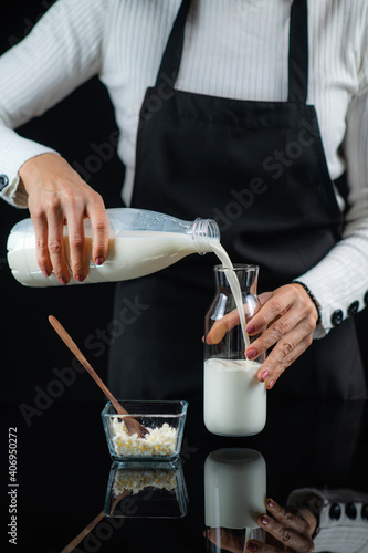 Pouring Milk into a Glass Bottle with Kefir Culture Grains. Making Homemade Kefir. Black Background. photo