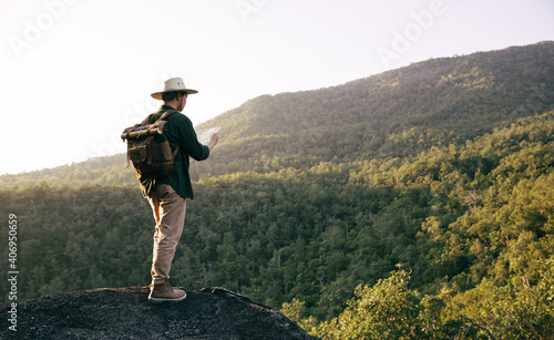Asian teenager using compass with paoer map to hike through forest to peak of mountain.