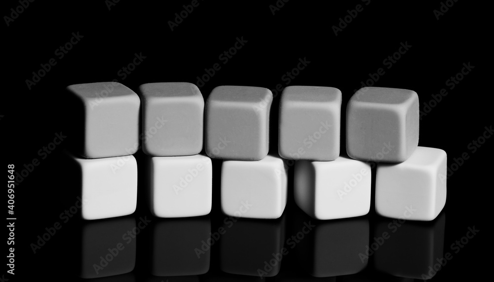 A pyramid of white and dark cubes on a black surface with a reflection. Close-up, isolated background, selective focus. A pyramid of white and dark cubes on a black surface with a reflection. Close-up, isolated background, selective focus.