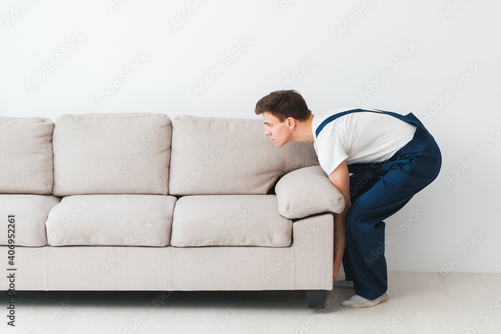 Loader moves sofa, couch. worker in overalls lifts up sofa, white background. Delivery service concept. Courier delivers furniture in case of move out, relocation. Loader moves sofa, couch. worker in overalls lifts up sofa, white background. Delivery service concept. Courier delivers furniture in case of move out, relocation.