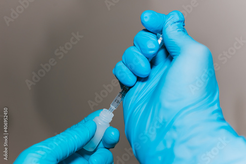 Close-up of hands with blue gloves holding a syringe and a small bottle. The concept of covid19 vaccination.