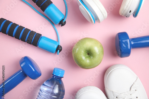 Fitness equipment. Apple, sneakers, water bottle, dumbbells, headphones on the pink background.