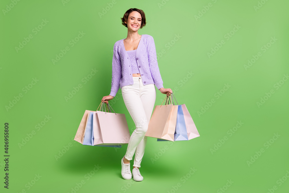 Full body photo of adorable cheerful person arms hold bags toothy smile isolated on green color background Full body photo of adorable cheerful person arms hold bags toothy smile isolated on green color background