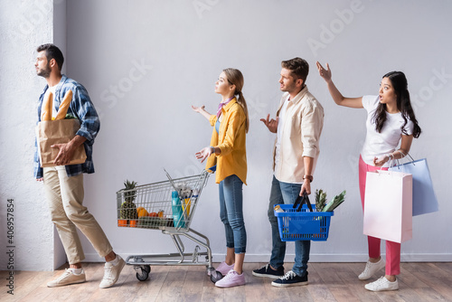 Foto Angry multicultural customers with purchases pointing with hands in queue