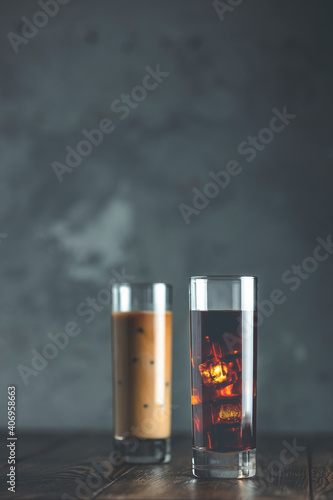 Two glasses of brew cold coffee and ice. Cold summer drink on a dark wooden table and gray background with copy space