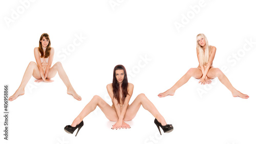 Three attractive young women with long hair sitting on the floor, their private parts are not visible, beauty concept, isolated in front of white studio background