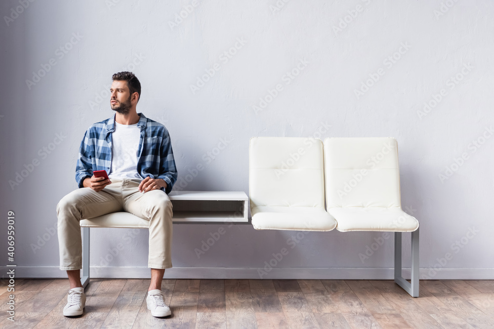 Man holding cellphone while sitting on chair in hall