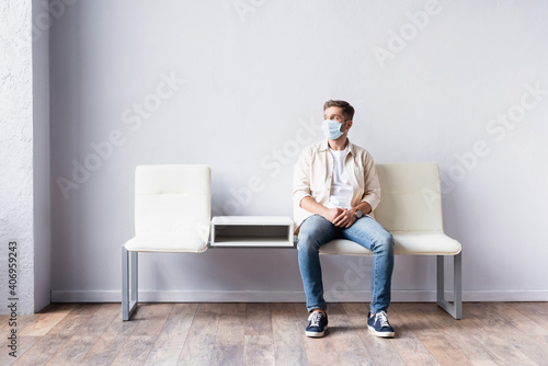 Young man in medical mask sitting in hall