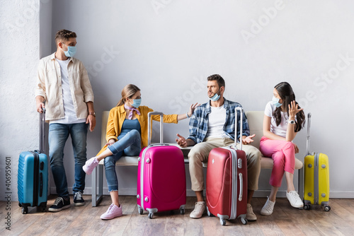 Multiethnic people in medical masks looking at confused man near baggage in airport