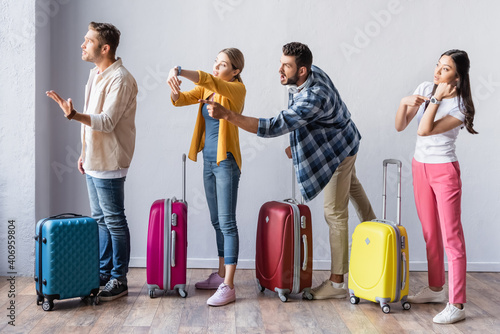 Aggressive multicultural people pointing at wristwatch near suitcases in airport