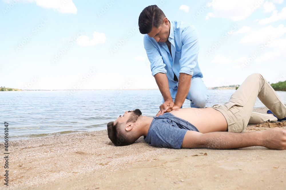 Passerby performing CPR on unconscious young man near sea. First aid Passerby performing CPR on unconscious young man near sea. First aid