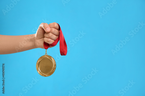Woman holding gold medal on light blue background, closeup. Space for text
