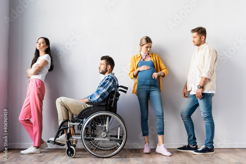Pregnant woman checking time near disabled man and multiethnic people in hall