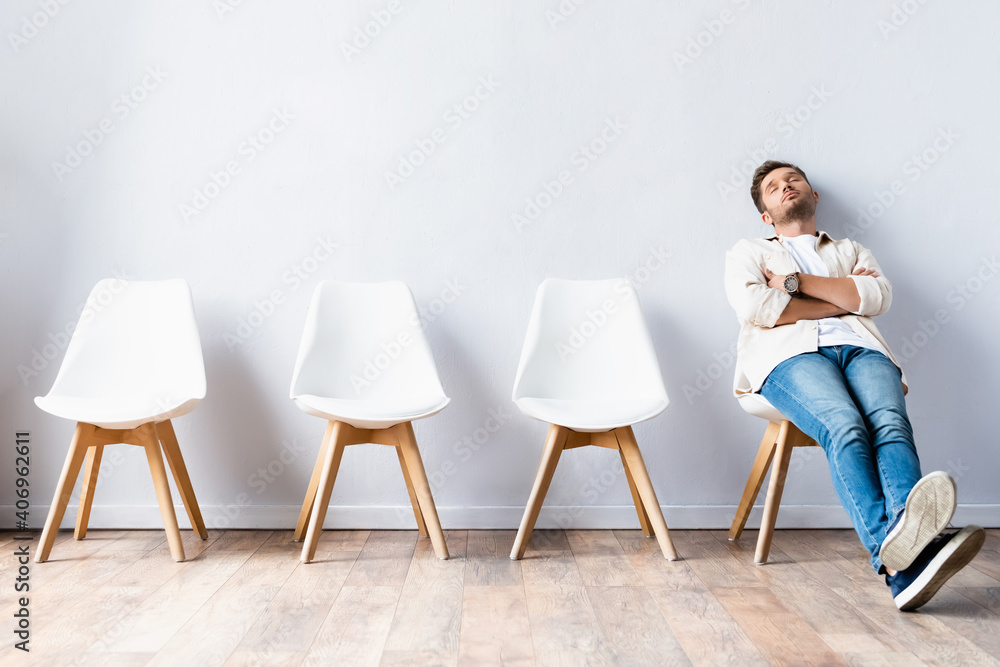 Tired man sitting with crossed arms near chairs in hall