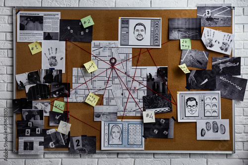 Detective board with fingerprints, photos, map and clues connected by red string on white brick wall photo