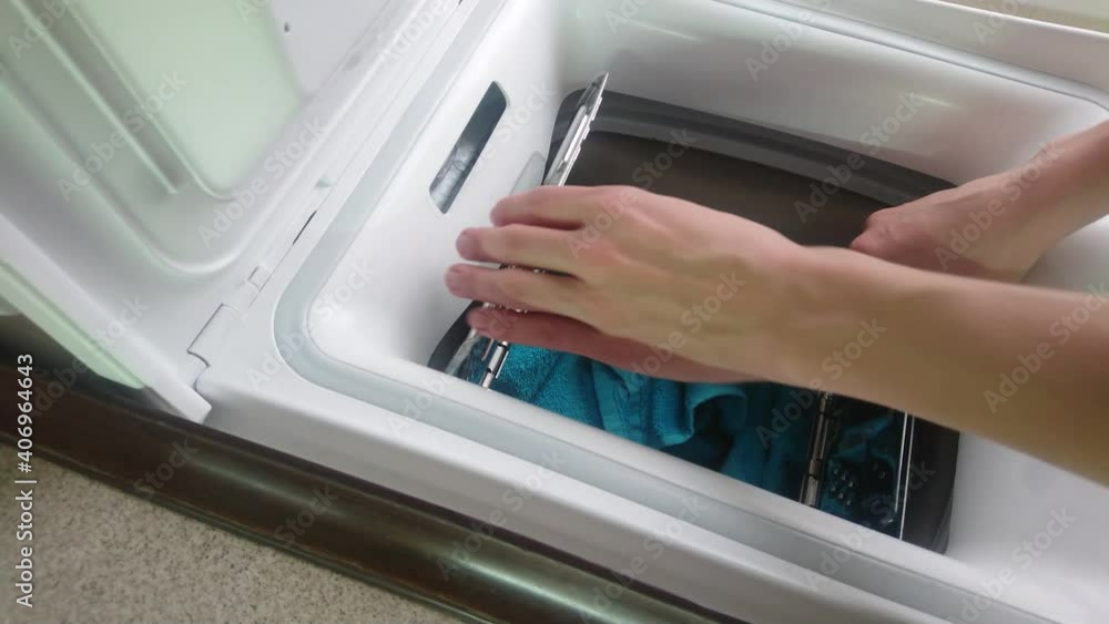 Woman loads dirty clothes into a vertical washing machine Woman loads dirty clothes into a vertical washing machine