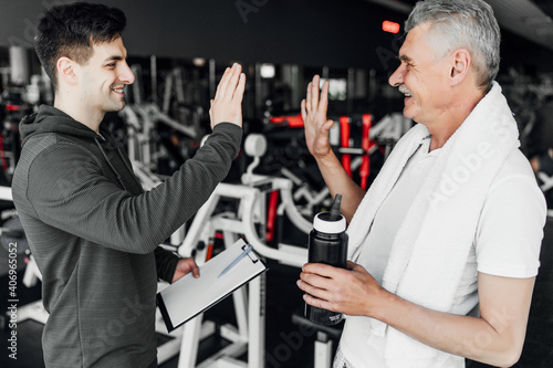 Senior man and his coach greet each other before training in the gym. Training plan. Rehabilitation