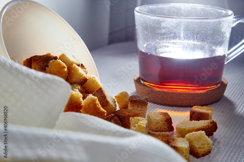 Square toasted pieces of homemade delicious rusk, hardtack, Dryasdust, zwieback on a plate and black tee in a cap on a white tablecloth. photo