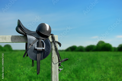 The bridle, the horse saddle and the riding helmet are on the wooden hitching post in outdoors.