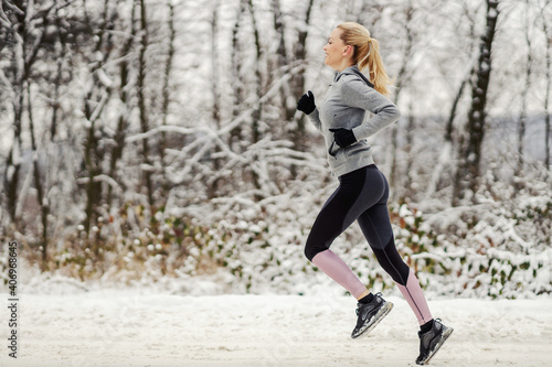 Sportswoman running fast on snowy trail in nature at winter. Winter fitness, outdoor fitness, chilly weather
