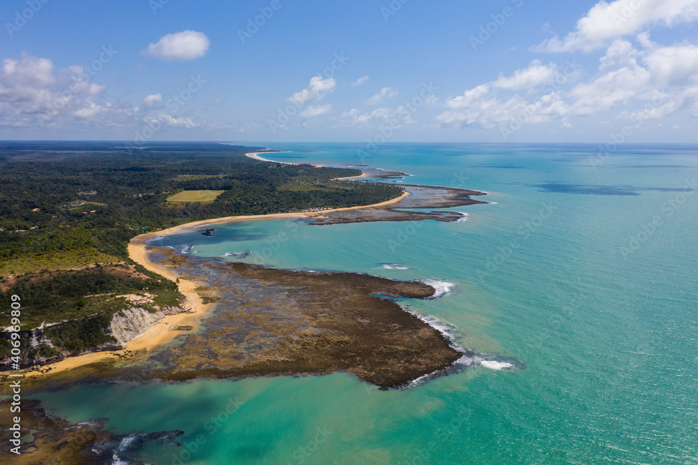 Aerial view of seashore cliff and blue sky with a few clouds on a sunny day. Green vegetation and trees. Coral reefs in the sea at Praia do Espelho beach, Bahia, Brazil. Post pandemic travel. Aerial view of seashore cliff and blue sky with a few clouds on a sunny day. Green vegetation and trees. Coral reefs in the sea at Praia do Espelho beach, Bahia, Brazil. Post pandemic travel.