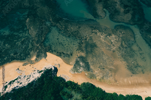 Top down aerial view of seashore and coral reefs close to tropical forest vegetation at Praia do Espelho, Bahia, Brazil. Nice green sea and golden brown sand. Post pandemic travel destination.