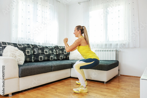 Smiling fit sportswoman doing squats at home. If you can't go to the gym, you can do exercises at home.