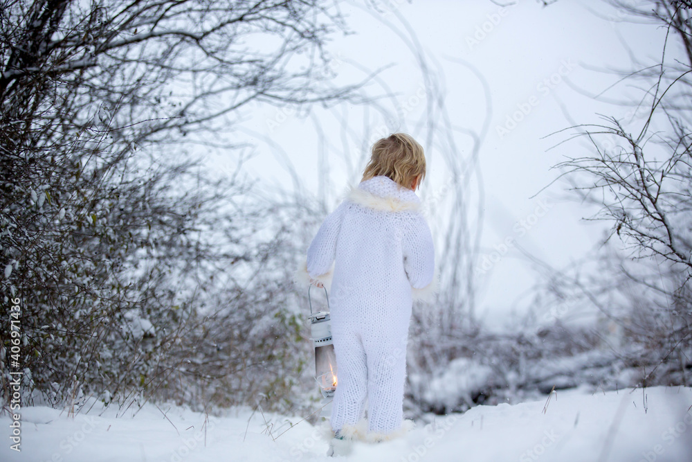 Beautiful blond toddler child, boy with white knitted handmade overall, holding lantern in the snow Beautiful blond toddler child, boy with white knitted handmade overall, holding lantern in the snow