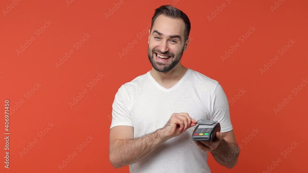 Smiling bearded young man 20s in white casual t-shirt isolated on orange background. People lifestyle concept. Hold wireless modern bank payment terminal to process and acquire credit card payments Smiling bearded young man 20s in white casual t-shirt isolated on orange background. People lifestyle concept. Hold wireless modern bank payment terminal to process and acquire credit card payments