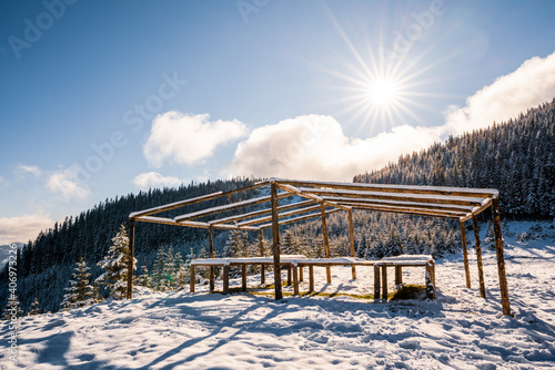 The gazebo on the top of the mountain stands in a snow-covered meadow  bathed in the light of the bright cold sun