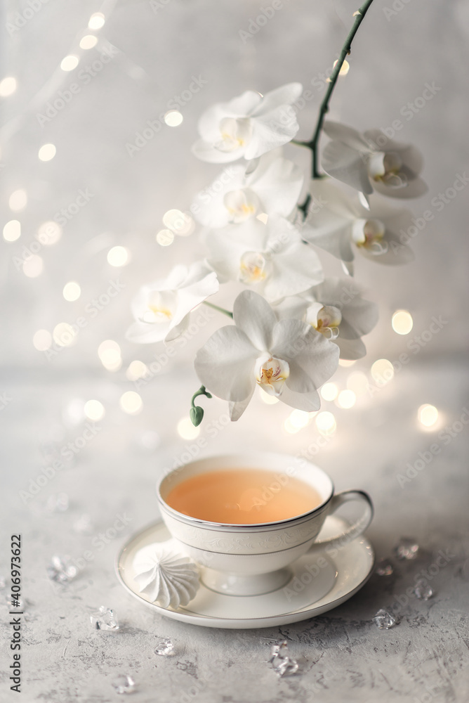 Cozy home spring breakfast still life. A porcelain cup of hot green tea with a marshmallow dessert on a gray background is decorated with a flowering branch of a white otchid. Spring concept. Cozy home spring breakfast still life. A porcelain cup of hot green tea with a marshmallow dessert on a gray background is decorated with a flowering branch of a white otchid. Spring concept.