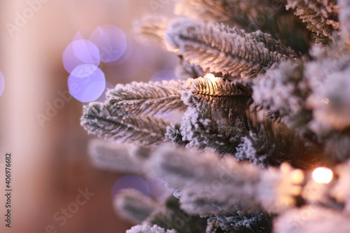 an artificial green spruce branch with garlands stands in the room and flashes warm white and purple light