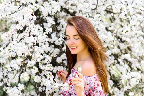 Portrait of beautiful red-haired young woman in white dress in spring flowers, blossom