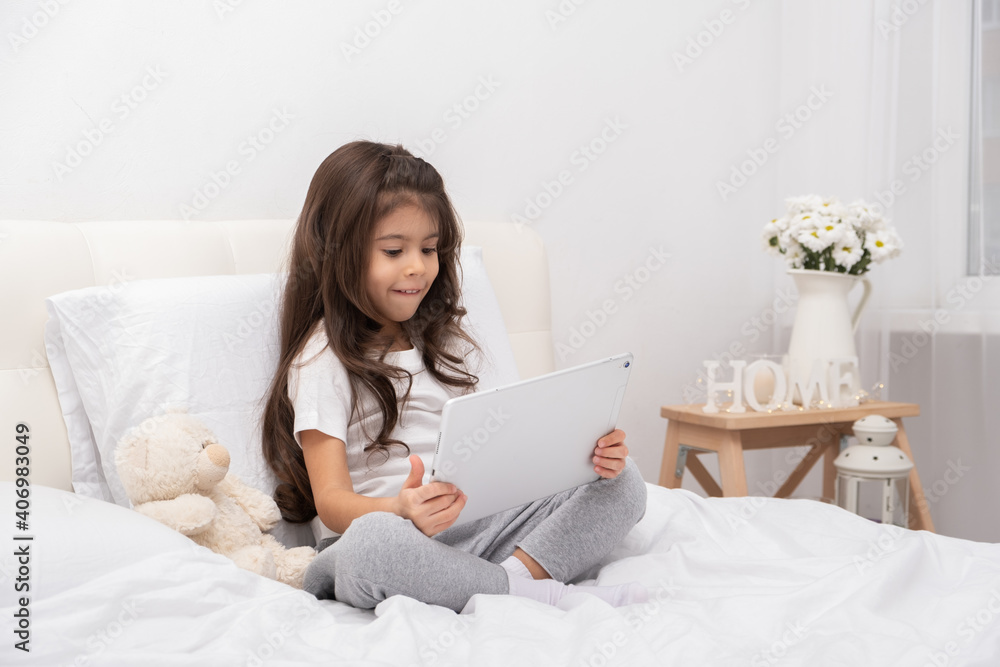 little girl in home wear with teddy bear using tablet sitting on bed little girl in home wear with teddy bear using tablet sitting on bed