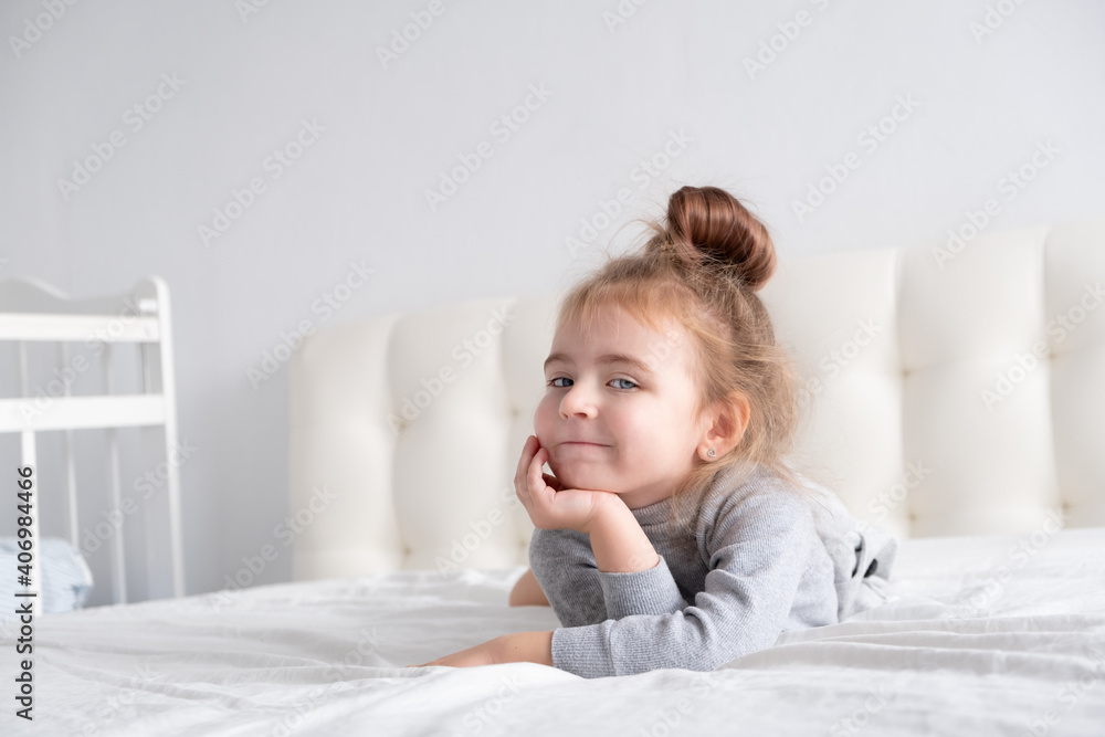 little girl in grey turtleneck having fun on white bedding little girl in grey turtleneck having fun on white bedding