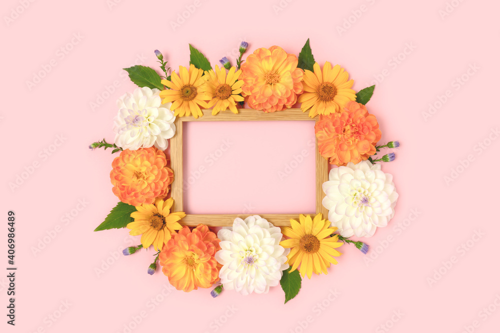 Top view of flower border frame made of dahlia, arnica and green leaves on a pink background. Greeting card template with copyspace.