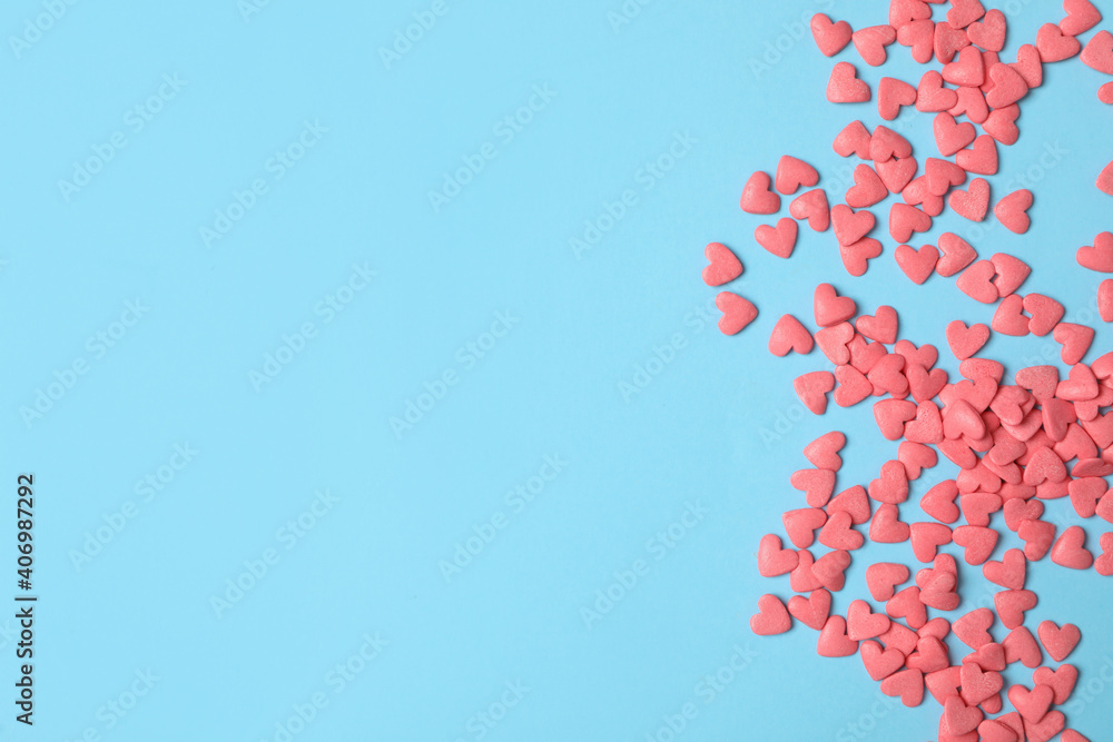 Bright heart shaped sprinkles on light blue background, flat lay. Space for text