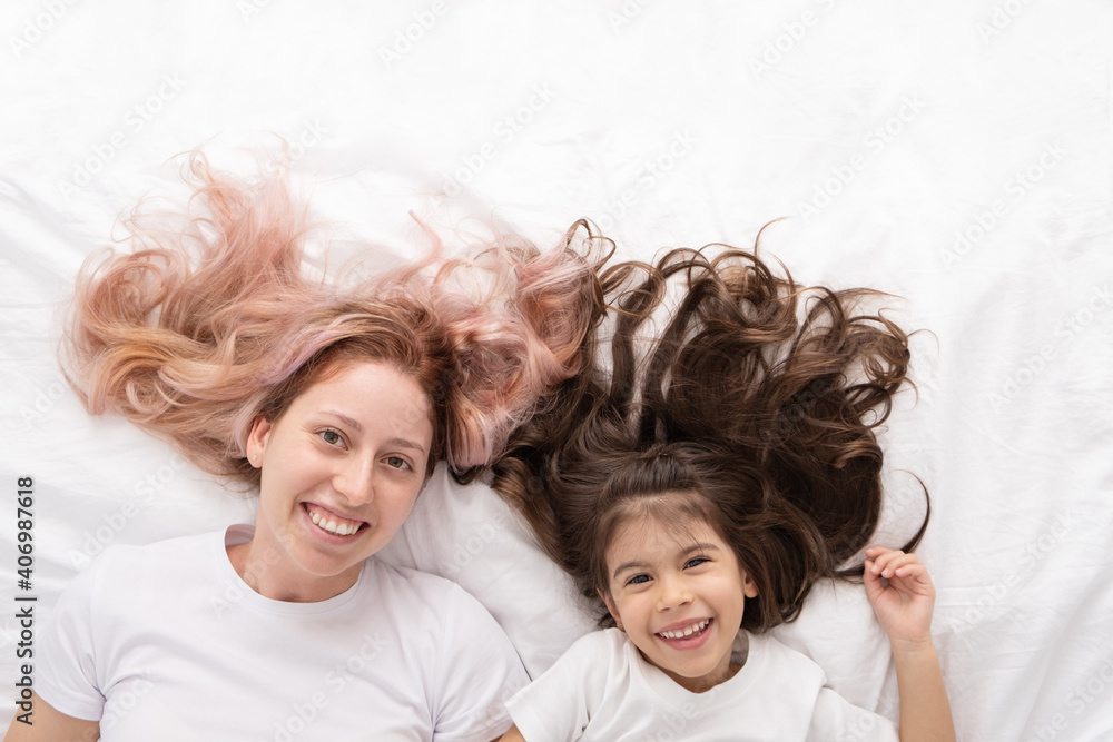 young mother and little active daughter lying in bed at home, having fun.