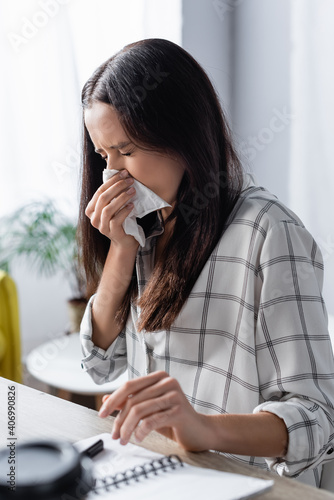 Quadro su tela young woman wiping nose with paper napkin while suffering from allergy on blurre