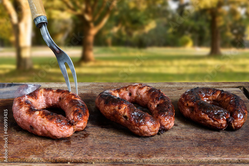 Sausage barbecue being cut on a wooden board. Background with trees and defocused field. Traditional barbecue from southern Brazil