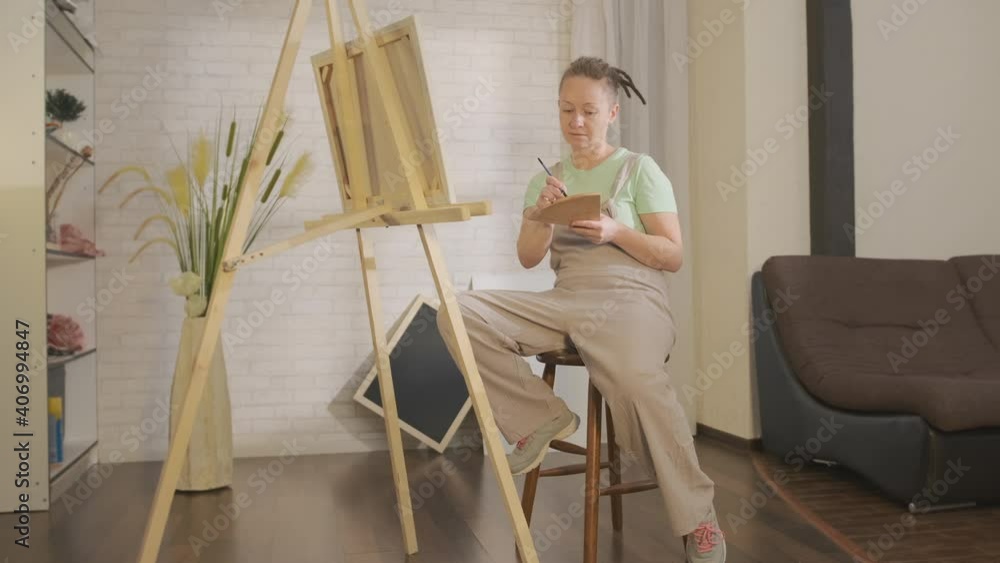 Contemporary artist paints picture in home studio. Stylish informal woman engaged in creative work. Contemporary artist paints picture in home studio. Stylish informal woman engaged in creative work.