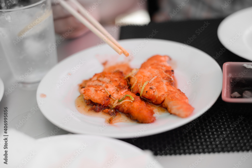 Fish salmon cutlets with sauce on white plate, hand with chopsticks. Food at buffet restaurant